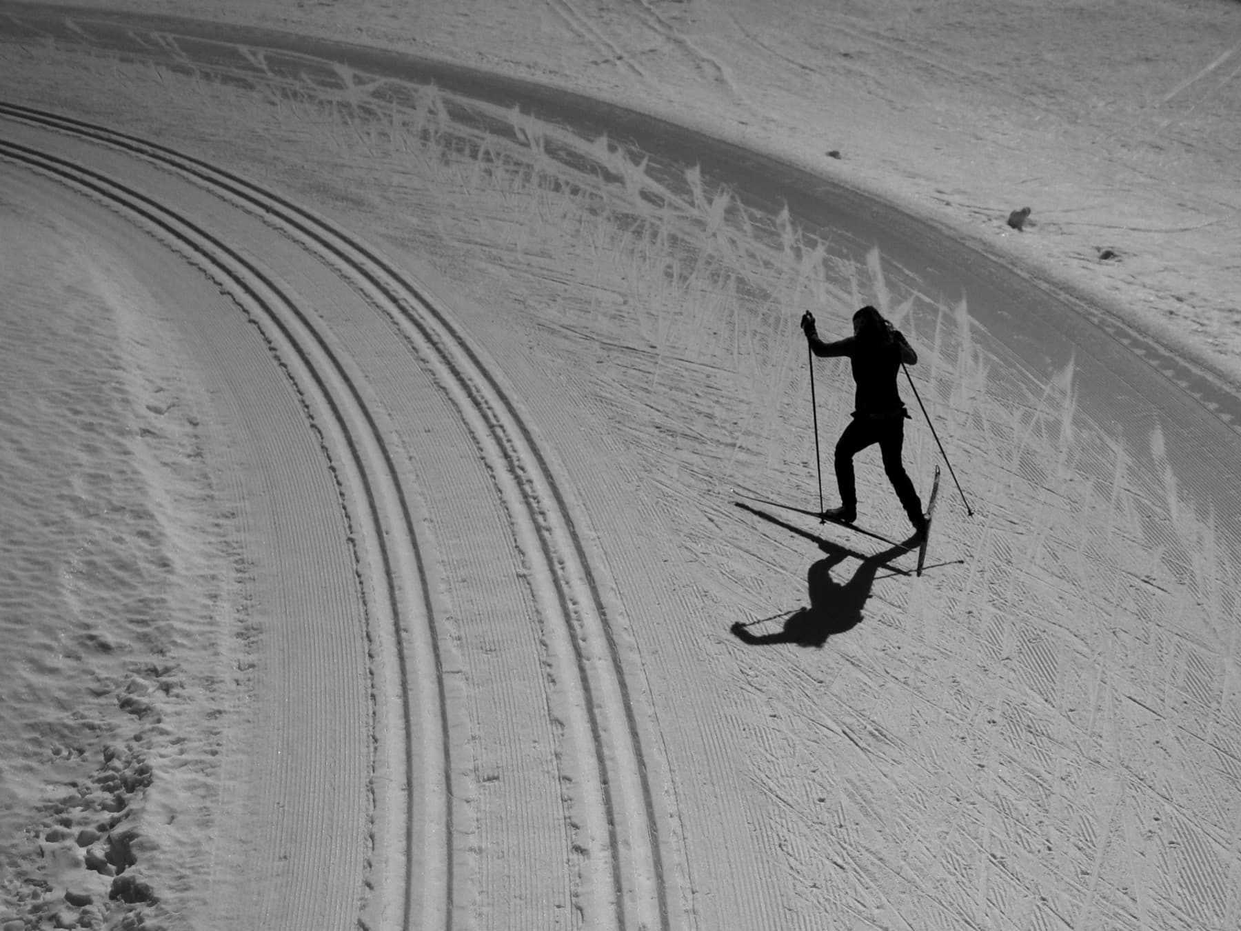 Black-and-white overhead view of a skier climbing beside groomed tracks
