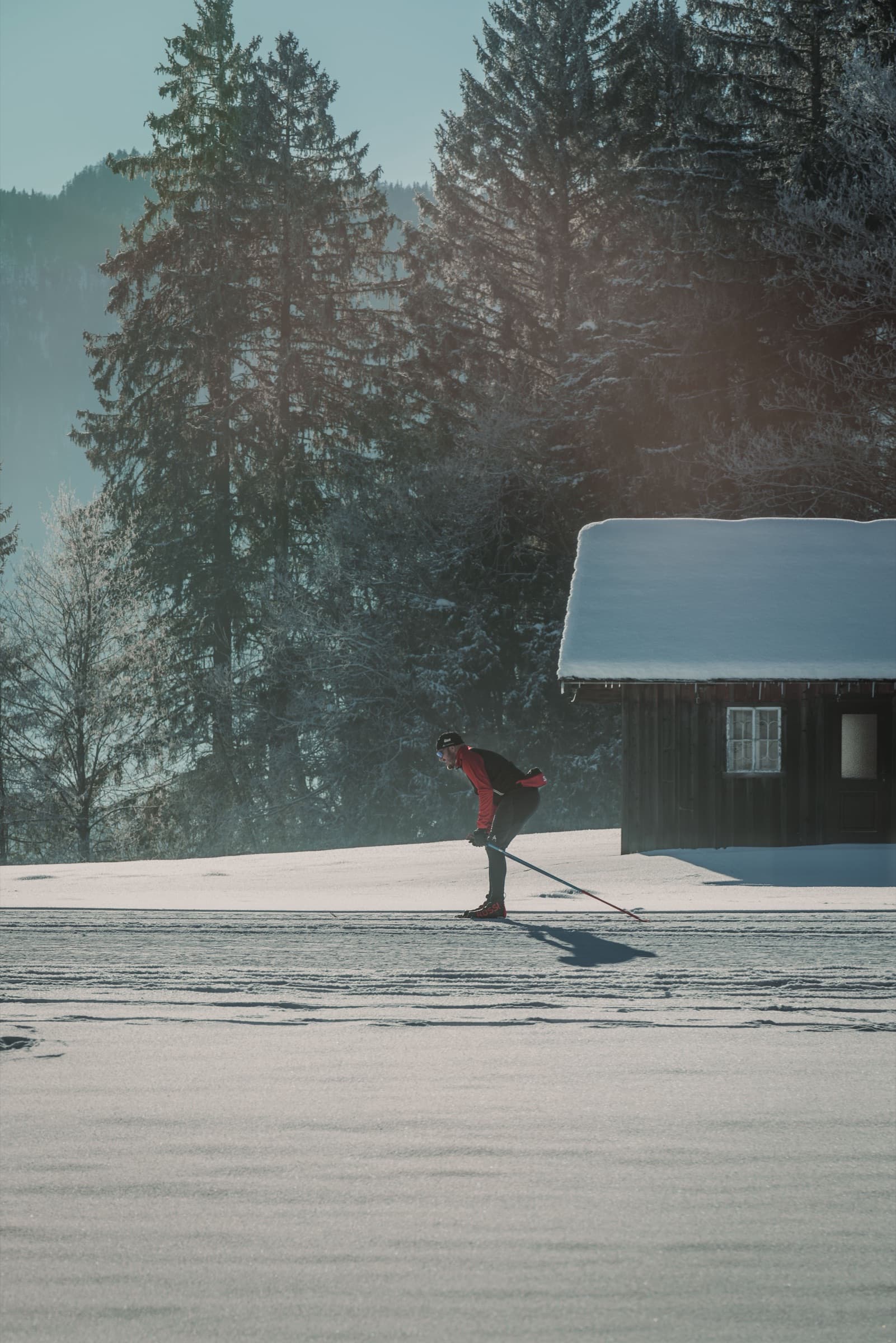 A skier in red striding past a snow-covered cabin