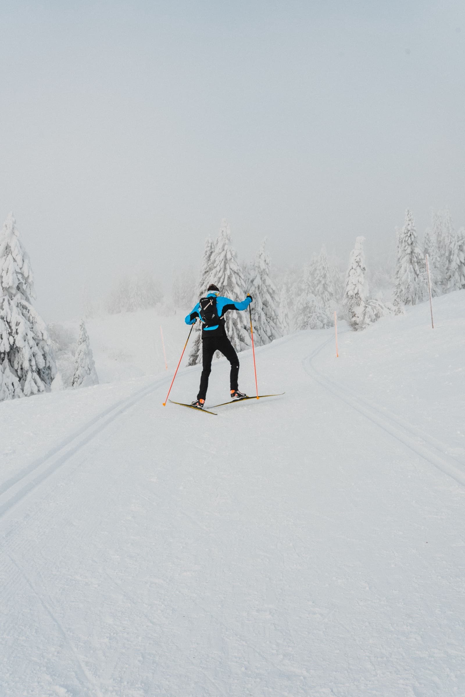 A skate skier in blue climbing a foggy groomed trail