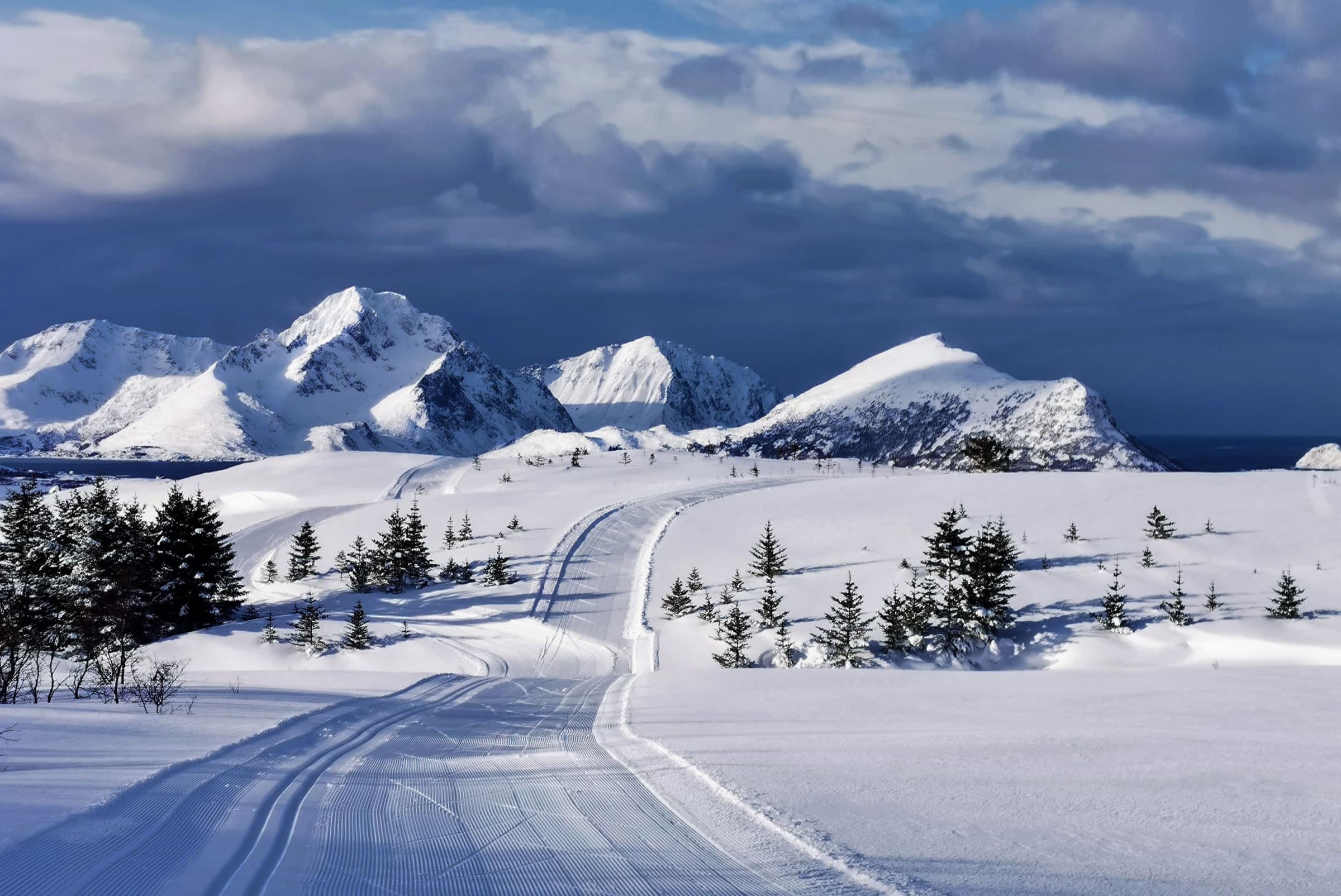 A groomed ski trail winding toward snowy coastal peaks